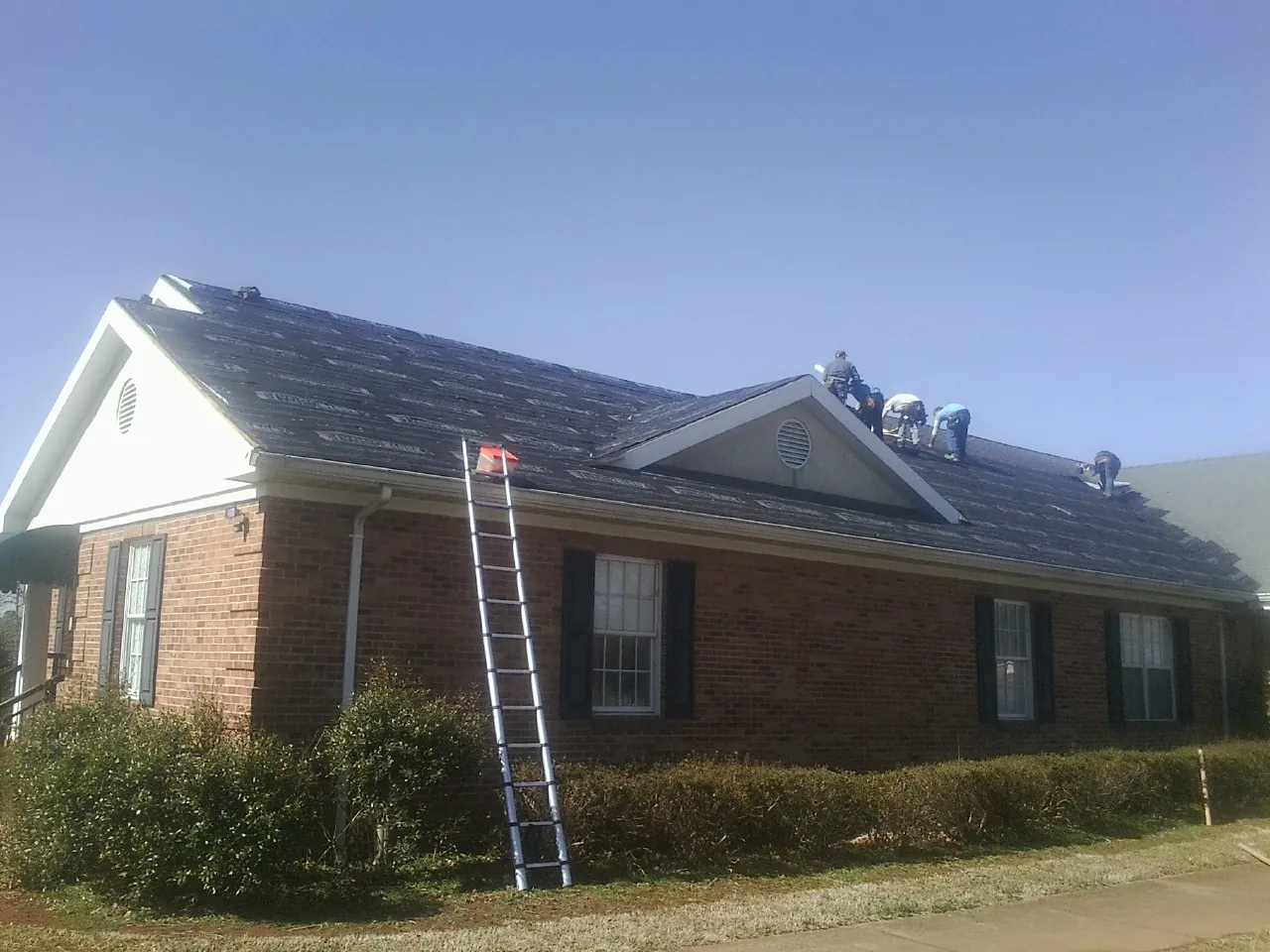 Crew tearing shingles off a brick ranch roof with a ladder set — Emergency Roof Repair work by our crew in Onslow