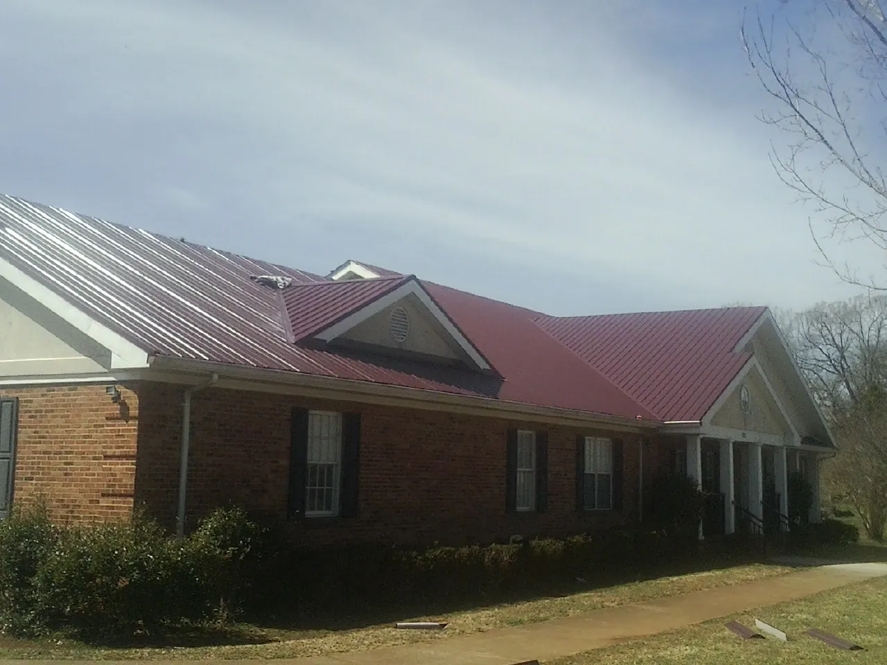 Red metal roof with gabled entries on a long brick building, from a Hail Damage Roof Repair job in Onslow