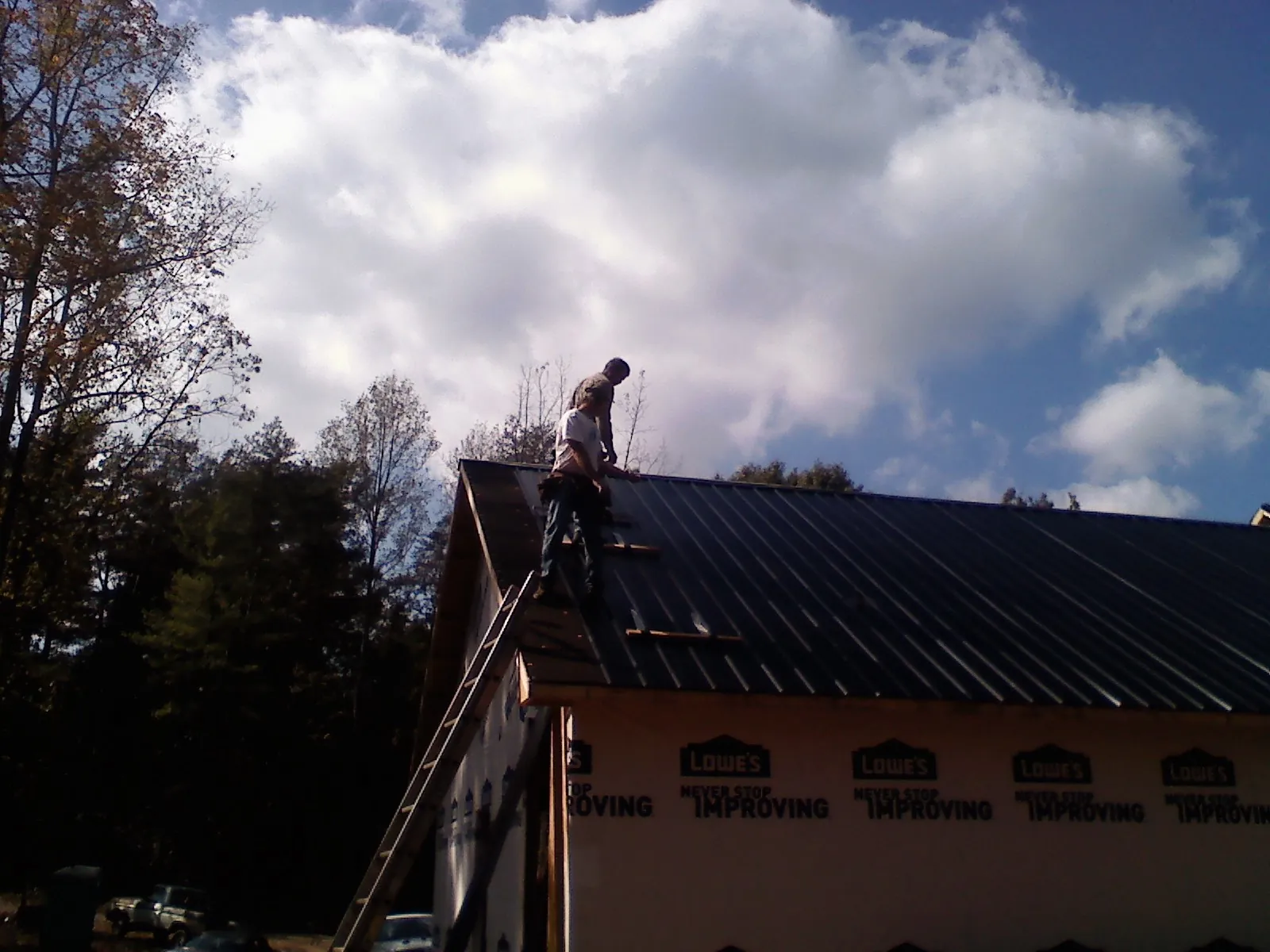 Roofer fastening dark metal panels high against a cloudy sky, from a Roof Inspection job in Onslow