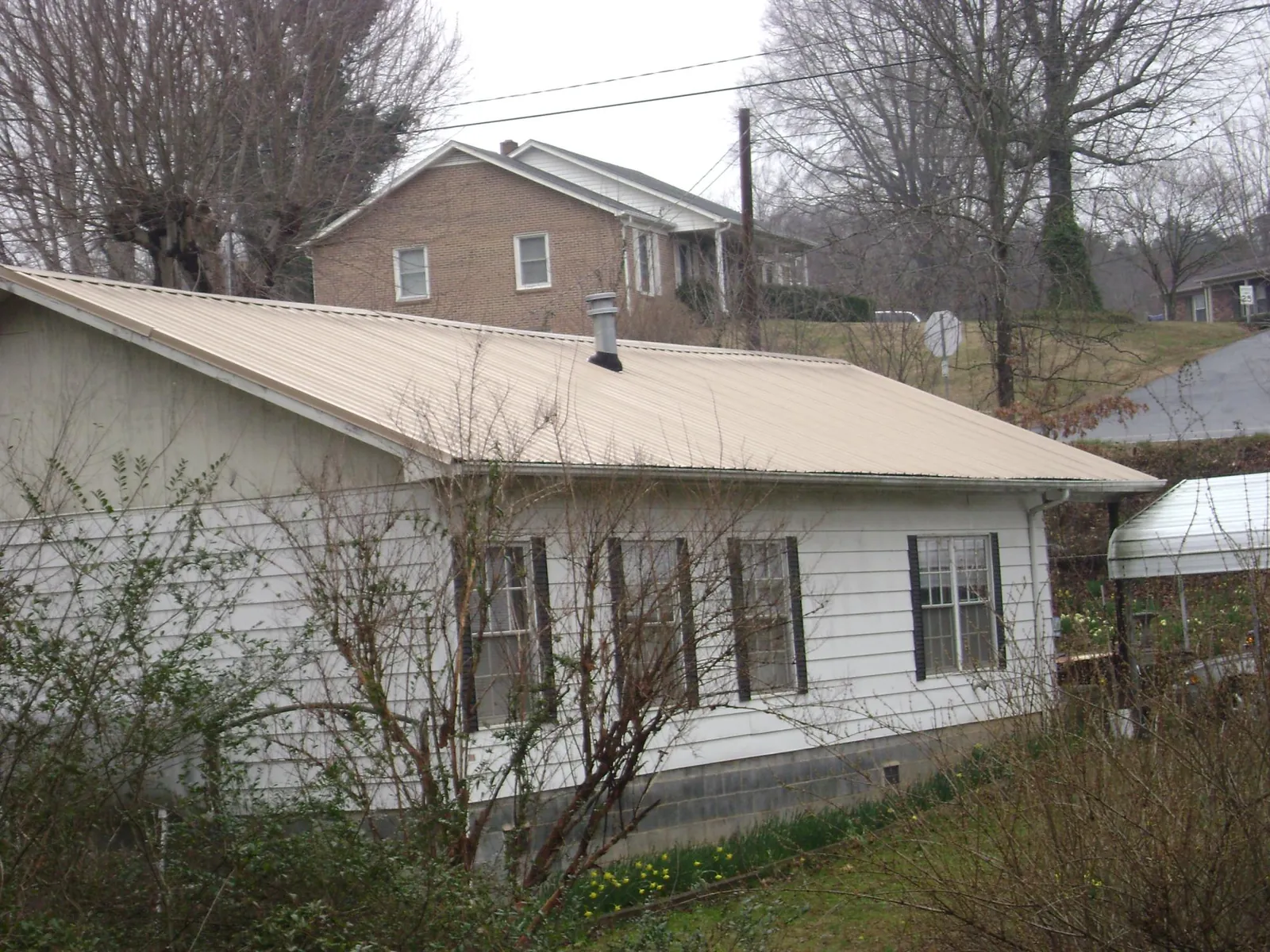 Tan metal roof on a white sided house set into a hillside — Commercial Roofing by Roofing Brothers in Onslow