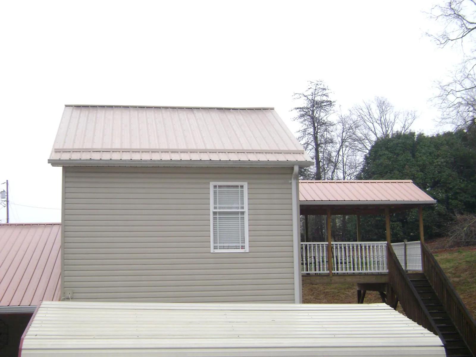 Tan metal roofs on a two story addition and attached porch, from a Roof Replacement job in Onslow